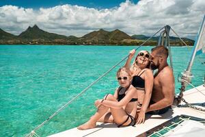 une content famille dans maillots de bain est assis sur une catamaran dans le Indien océan. portrait de une famille sur une yacht dans le corail récif de maurice photo