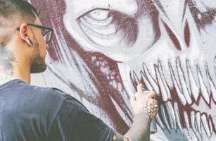 rue graffiti artiste La peinture avec une Couleur vaporisateur une foncé monstre crâne graffiti sur le mur - urbain, mode de vie rue art concept - concentrer sur le sien main photo