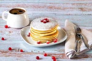 Matin petit déjeuner de Crêpes avec canneberges et en poudre sucre et une tasse de café sur une en bois table photo