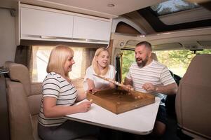 une famille de Trois est en jouant une planche Jeu tandis que séance dans une camping car photo