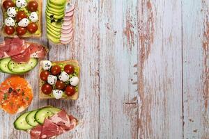 un assortiment de des sandwichs avec poisson, fromage, Viande et des légumes allonger sur le en bois table photo