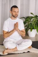 une homme dans blanc tenue de sport est Faire yoga avec une aptitude chambre. le concept de une en bonne santé mode de vie photo