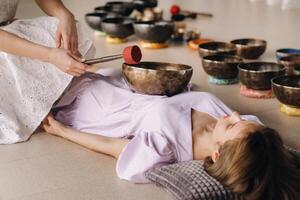 le cuivre en chantant bol de le népalais Bouddha dans le spa. une Jeune magnifique femme est Faire une massage avec en chantant boules dans une spa salon contre le toile de fond de une cascade photo