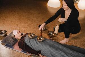 une Jeune magnifique femme est Faire une massage avec en chantant boules et une koshi cloche à un autre fille. du son thérapie photo