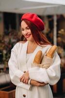 portrait de une jolie femme dans une rouge béret et une blanc cardigan avec baguettes dans sa mains ambulant par le l'automne ville photo