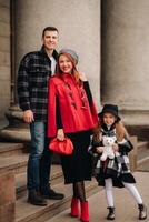 une élégant famille de Trois est dans ville dans le automne, et le fille avec le farci jouet est de bonne humeur photo