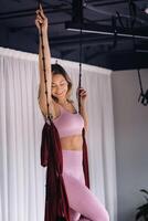 une femme dans rose vêtements Est-ce que yoga sur une suspendu Bourgogne hamac dans une brillant Gym photo