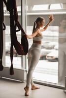 portrait de une fille dans blanc tenue de sport permanent près le fenêtre et en portant une pendaison hamac dans sa main dans le aptitude pièce photo