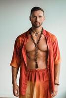 une musclé homme avec une nu torse dans Orange vêtements des stands dans une pièce sur une lumière Contexte photo