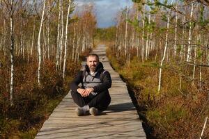 une homme est assis sur une en bois chemin dans une marais dans Elnya, biélorussie photo