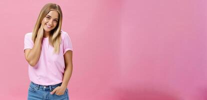 portrait de timide et timide attrayant européen femme avec juste cheveux dans décontractée tenue émouvant cou idiot basculant tête et souriant mignonne à caméra permanent plus de rose Contexte photo