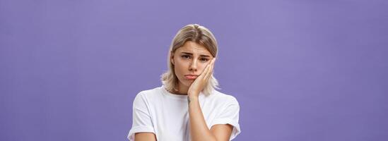 à la taille coup de malheureux misérable et triste mignonne blond femelle dans blanc décontractée T-shirt pincer lèvres penché visage sur paume et renfrogné de déception et le regret plus de violet Contexte photo