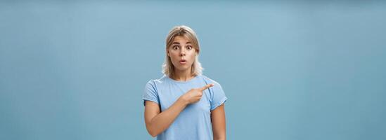 studio coup de étonné étourdi mignonne blond témoin incroyable un événement halètement ouverture bouche regarder étonné et montrer du doigt la gauche étant interrogé et sous le choc plus de bleu Contexte photo