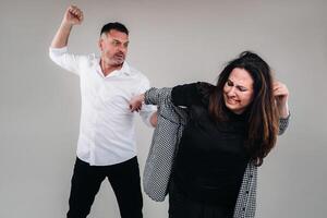 une homme oscillations le sien poing à une battu femme permanent sur une gris Contexte. national la violence photo