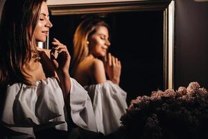 magnifique fille dans le miroir réflexion à maison. fille avant le vacances près le Accueil miroir.a fille dans une blanc robe avec longue cheveux est Aller à une fête à Accueil photo