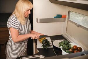 une femme cuisine nourriture dans le cuisine à l'intérieur une camping car, le intérieur de une camping car photo