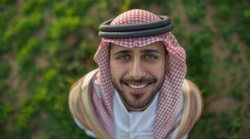 ai généré arabe homme à la recherche en haut à le caméra souriant, portant traditionnel vêtements photo