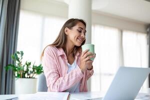 positif Jeune femme pigiste en train de regarder vidéo dans Blog sur netbook et ayant une café à confortable bureau. magnifique Jeune affaires femme travail sur ordinateur portable.freelancer de liaison à l'Internet photo