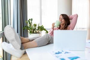 Jeune jolie femme d'affaires dans le Bureau séance dans Bureau chaise, mains en haut et avec sa pieds en haut sur une bureau profiter café photo