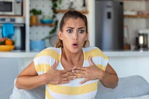 stressé Jeune femme sentiment douleur et émouvant poitrine souffrir de chagrin maladie à Accueil tandis que ayant cœur attaque, infarctus photo