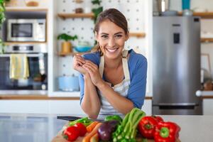 mignonne content Jeune brunette femme dans bien ambiance en train de préparer une Frais végétalien salade pour une en bonne santé la vie dans le cuisine de sa maison. photo