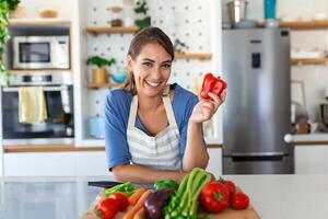 mignonne content Jeune brunette femme dans bien ambiance en train de préparer une Frais végétalien salade pour une en bonne santé la vie dans le cuisine de sa maison. photo