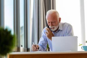 mature homme d'affaire travail sur portable et parlant sur téléphone portable. Beau mature affaires chef séance dans une moderne Bureau photo