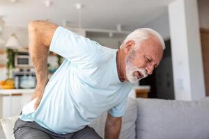 Sénior personnes âgées homme émouvant le sien dos, Souffrance de mal au dos, sciatique, sédentaire mode de vie concept. colonne vertébrale santé problèmes. soins de santé, Assurance photo