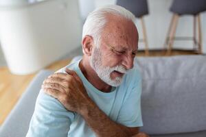 Sénior personnes âgées homme émouvant le sien épaule, Souffrance de épaule douleur, sciatique, sédentaire mode de vie concept. épaule santé problèmes. soins de santé, Assurance photo