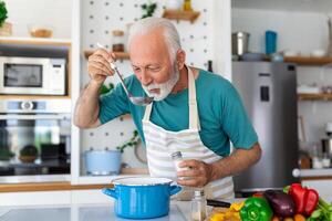 content retraité Sénior homme cuisine dans cuisine. retraite, loisir gens concept. portrait de souriant Sénior homme en portant cuillère à goût nourriture photo