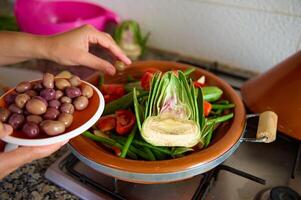 fermer femme au foyer ajouter Olives dans une repas tandis que cuisine en bonne santé végétarien repas dans tajine photo