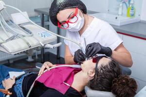 dentiste examiner les dents de une Jeune femme patient dans une dentaire clinique. dentisterie concept. dentiste et patient dans le dentaire bureau. photo