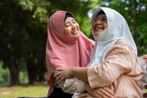 musulman prudent soignant ou infirmière prise se soucier de le patient dans le hôpital parc. content musulman mère dans hijab étreindre fille. concept de des économies et Sénior santé assurance, une content famille photo