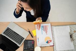 occupé et fatigué femme d'affaires en mangeant pain et Lait pour le déjeuner à le bureau Bureau et travail à livrer financier déclarations à une chef. surmené et mauvais pour la santé pour prêt repas, Burnout concept. photo