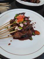 photo de chèvre satay avec noir soja sauce sur une blanc assiette