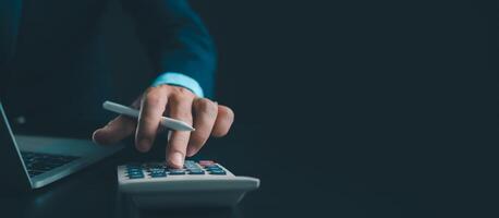 homme d'affaire dans noir costume travail sur portable ordinateur et tablette et calculatrice, main mains toucher sur tablette à Bureau avec foncé arrière-plan, en ligne fonctionnement, proche en haut, copie espace. photo