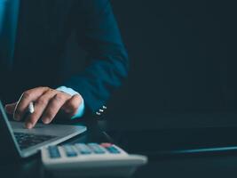 homme d'affaire dans noir costume travail sur portable ordinateur et tablette et calculatrice, main mains toucher sur tablette à Bureau avec foncé arrière-plan, en ligne fonctionnement, proche en haut, copie espace. photo