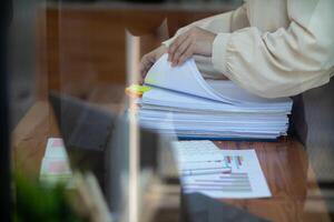 secrétaire est recherche par pile de important les documents sur Bureau table livrer leur à directeur pour présentation dans temps à réunion. concept de difficulté découverte information de piles de document photo