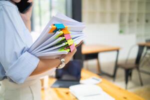 une Jeune secrétaire est recherche par le pile de les documents sur sa bureau à préparer pour un exécutif réunion. le secrétaire regardé épuisé de recherche par le pile de les documents sur sa bureau. photo