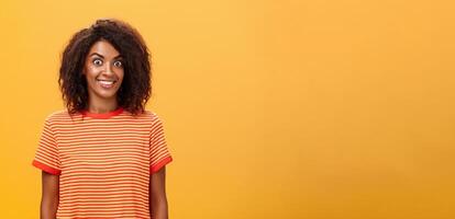 à la taille coup de étonné et excité charmant africain américain femme avec frisé coiffure éclater yeux de frisson et joie souriant largement étant surpris par génial cadeau plus de Orange Contexte photo