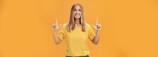 portrait de optimiste joyeux magnifique Jeune caucasien fille avec bronzer et juste cheveux à la recherche et montrer du doigt en haut, souriant gaiement en train de regarder feux d'artifice posant amusé et content contre Orange Contexte photo