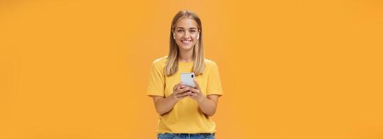 portrait de amical charismatique et sortant beau Jeune femelle dans Jaune T-shirt en portant téléphone intelligent portant sans fil écouteurs profiter écoute la musique sur façon à aptitude Gym photo