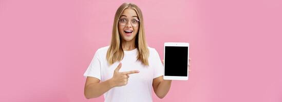 fille suggère acheter numérique tablette pour Université et oublier papier livres. excité content et Enchanté Jeune femelle étudiant dans blanc T-shirt et des lunettes montrer du doigt à dispositif écran recommander gadget photo