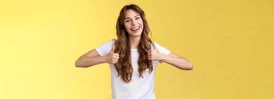 sortant positif sur de soi animé Jeune fille longue frisé la Coupe de cheveux soutien génial effort spectacle les pouces en haut positif réponse approuvant bien choix comme votre tenue souriant largement Jaune Contexte photo