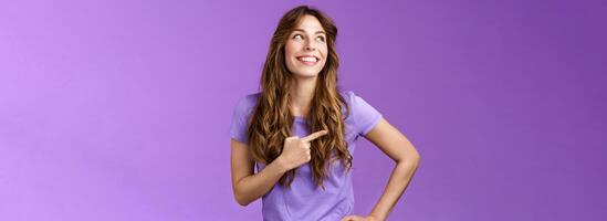 de bonne humeur motivée enthousiaste optimiste aux cheveux bouclés fille tour la gauche montrer du doigt de côté contempler produire bien choix souriant Enchanté ayant parfait été journée supporter violet Contexte photo