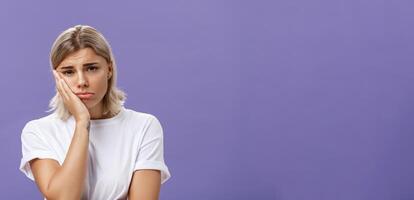 à la taille coup de malheureux misérable et triste mignonne blond femelle dans blanc décontractée T-shirt pincer lèvres penché visage sur paume et renfrogné de déception et le regret plus de violet Contexte photo