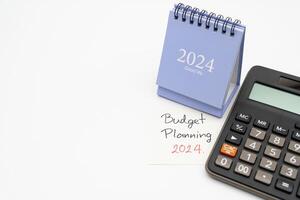 budget Planification 2024 texte message par main l'écriture sur papier note, calendrier 2024 et calculatrice. budget Planification concept. isolé sur blanc Contexte. photo