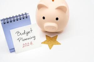 budget Planification 2024 texte message par main l'écriture sur papier note, calendrier, d'or étoile et porcin banque. budget Planification concept. photo