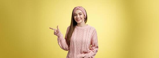 mode de vie, personnes, montrer du doigt concept. attrayant Jeune fille avec longue tout droit cheveux portant chandail montrer du doigt de côté en utilisant avant doigt, indiquant copie espace souriant joyeux, positif plus de Jaune mur photo