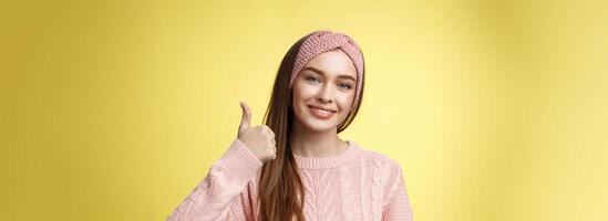 jolie européen Jeune fille dans Bandeau, rose chandail souriant ravi, heureux montrant les pouces en haut dans accord, approbation, donnant bien recommandation, aimer intéressant génial idée souriant de bonne humeur photo